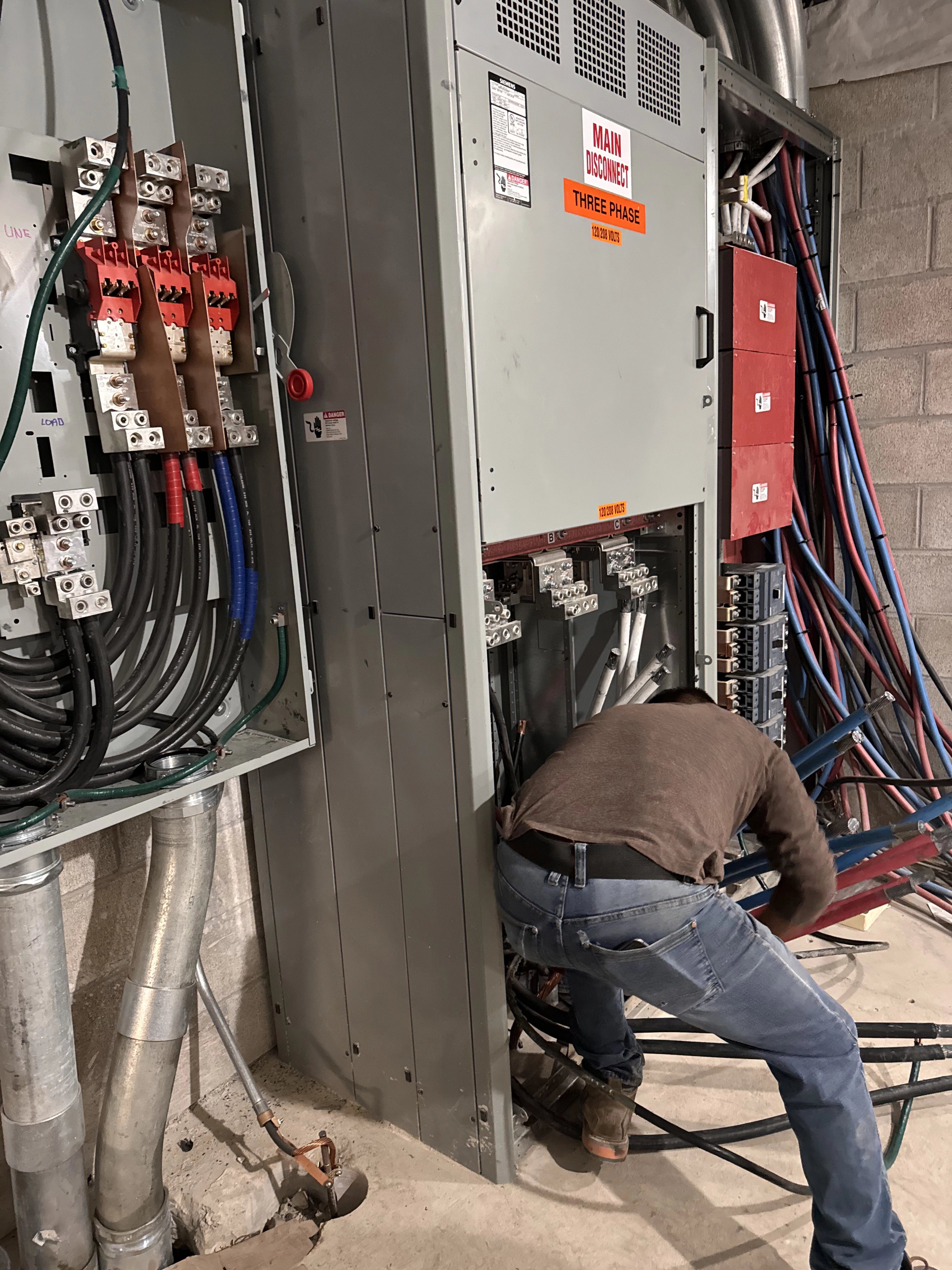 Electrician working on indoor large electrical box labeled; Main, Three Phase