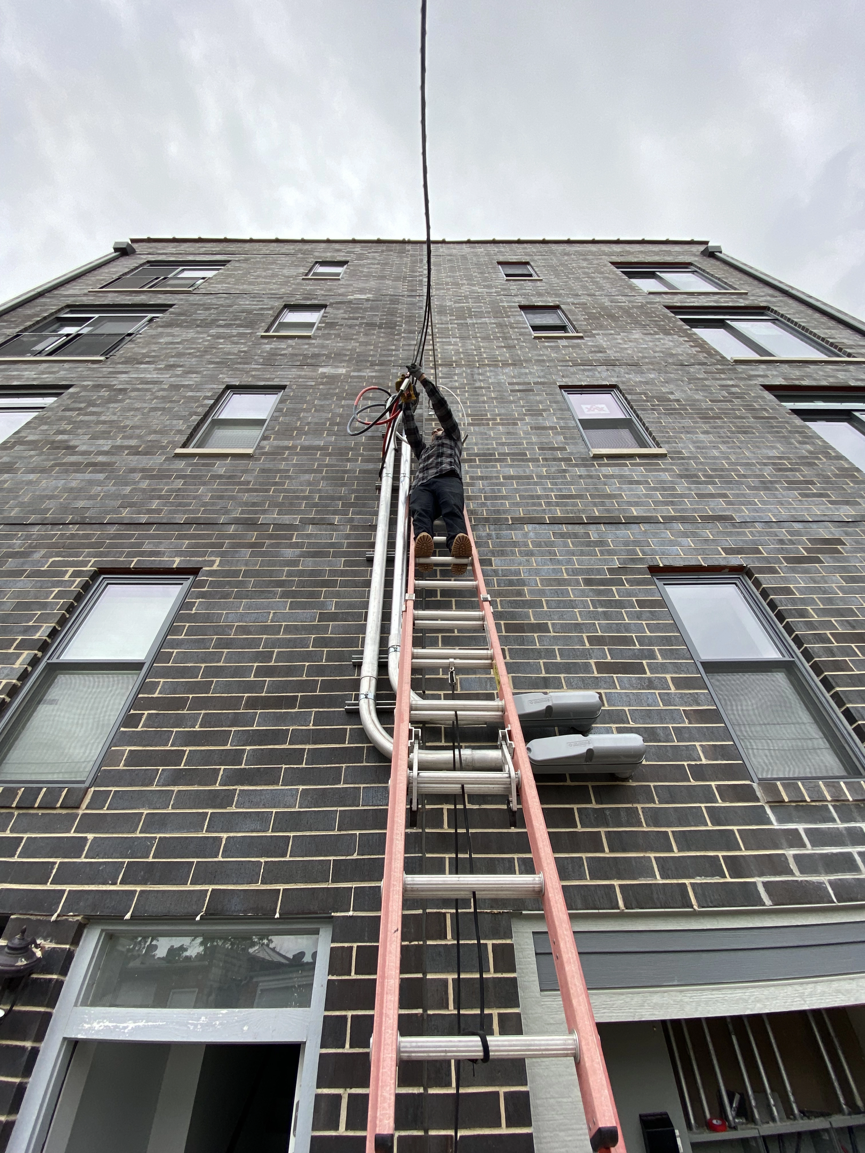 Electrician on ladder against an apartment complex connecting wires